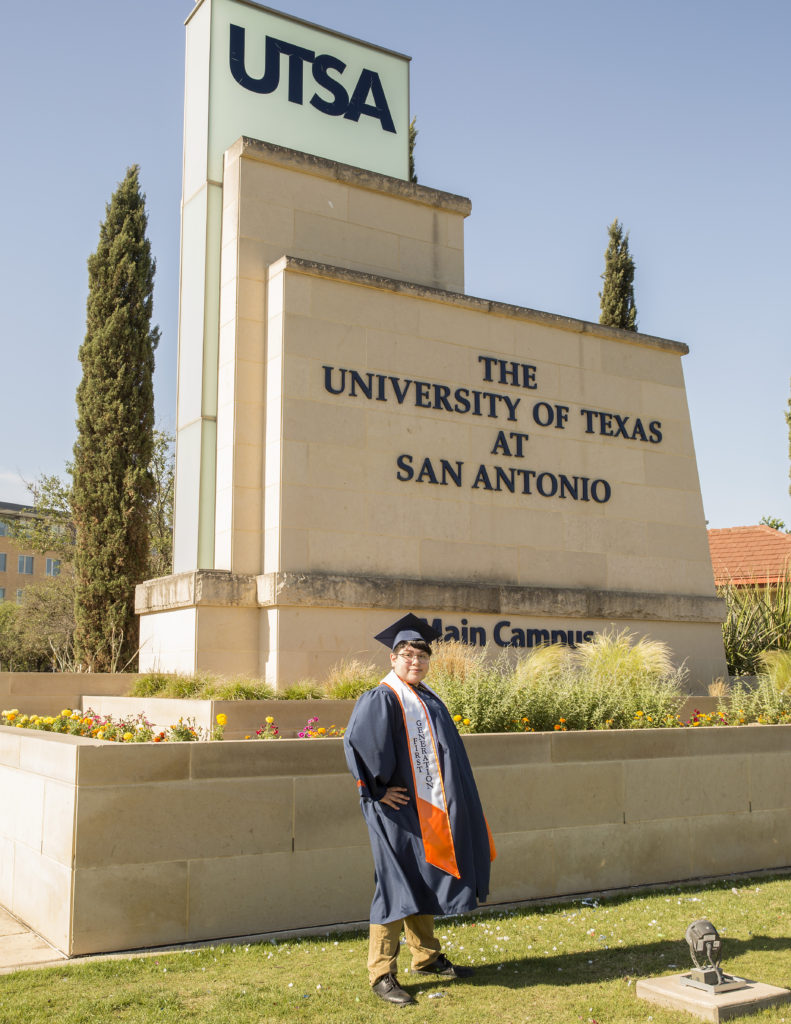 Senior Portrait of UTSA student in graduating cap and gown in from of UTSA sign